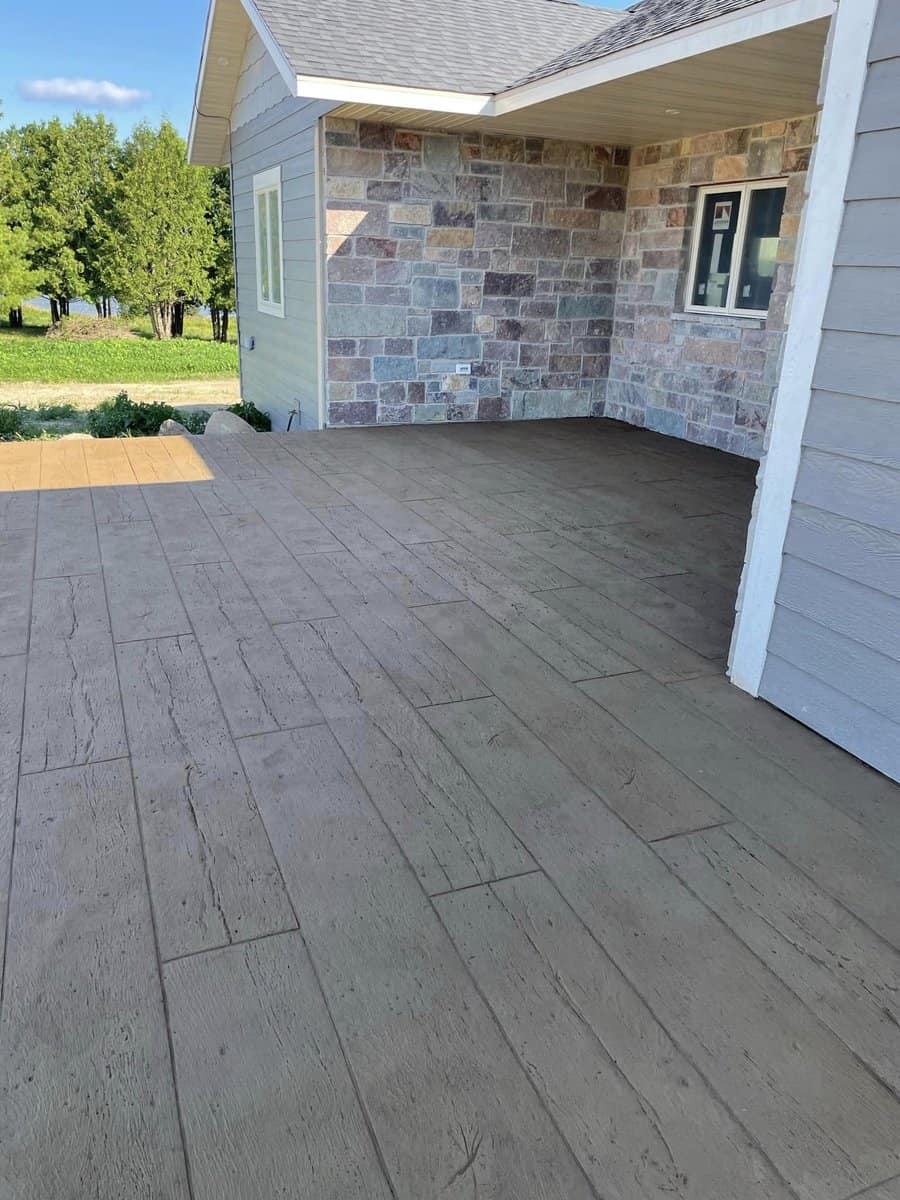 A residential porch with stamped concrete flooring and a stone veneer wall on a sunny day.