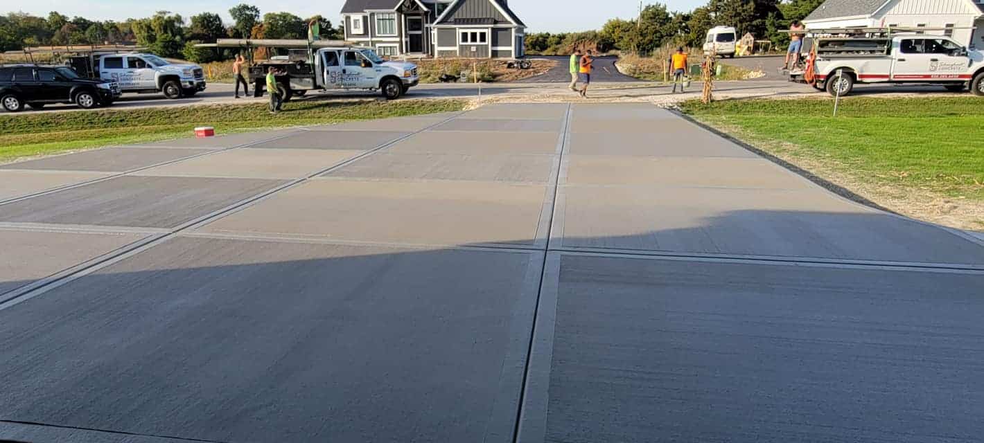 Freshly poured concrete driveway with construction workers and vehicles in the background.
