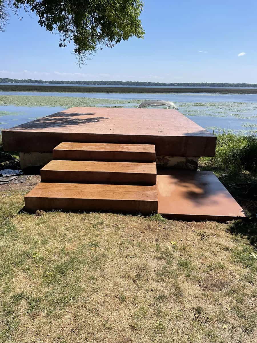 A concrete platform with steps leading down to a body of water, partially covered with aquatic plants, under a clear blue sky.