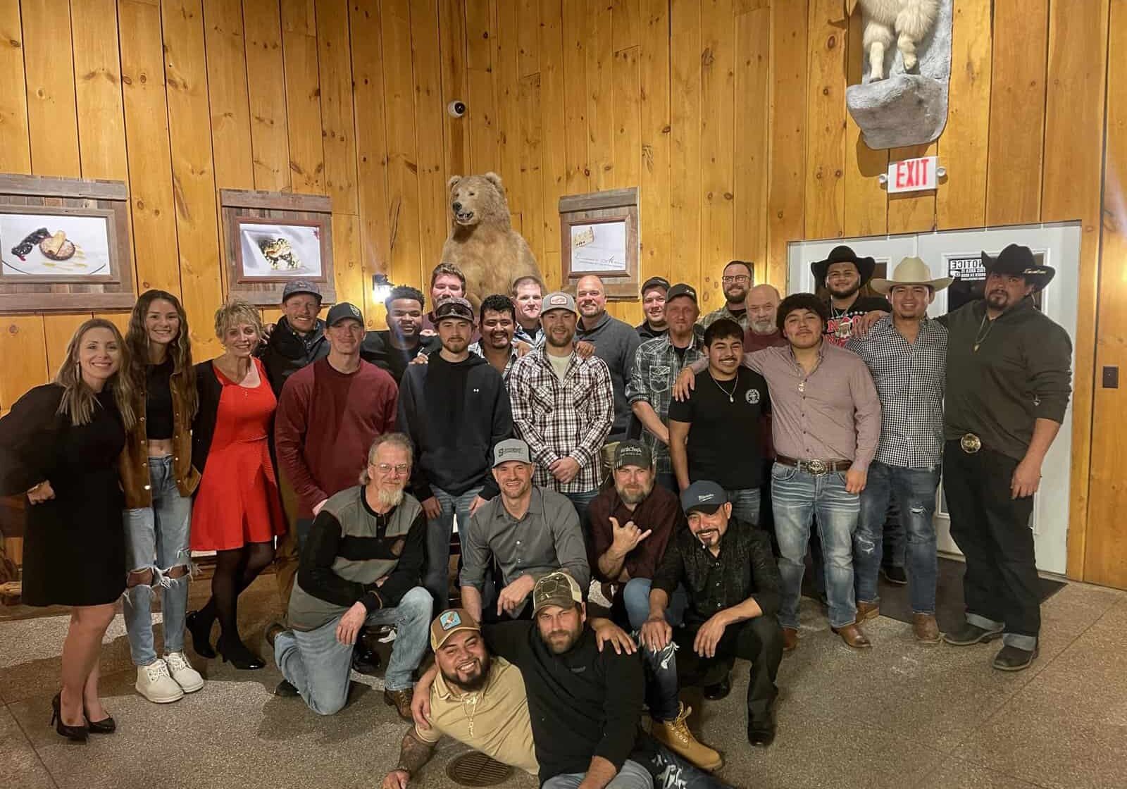 A large group of people posing for a photo in a room with wood paneling and wildlife art on the walls.